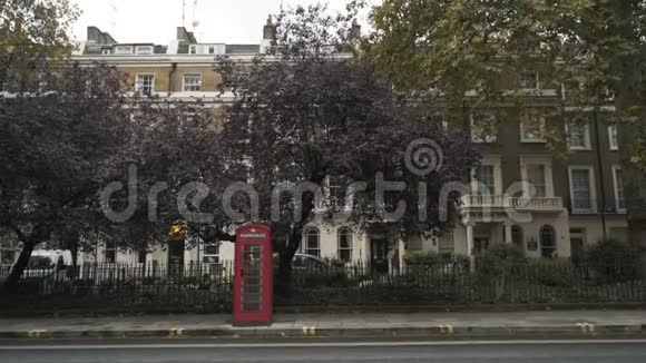 伦敦传统的红色电话亭站在靠近马路的街道上靠在树上国家标志视频的预览图
