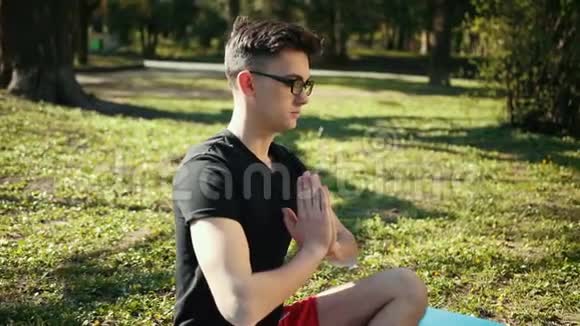 戴眼镜的年轻人双手合十练习冥想苏哈萨纳坐姿坐在地毯上的人视频的预览图