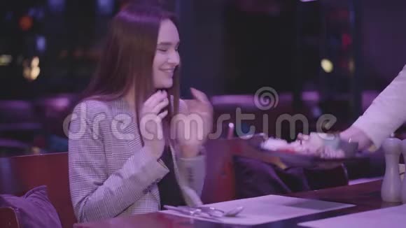 侍者给一个坐在一家昂贵餐馆的桌子旁的漂亮女孩带来了一道美味的菜视频的预览图