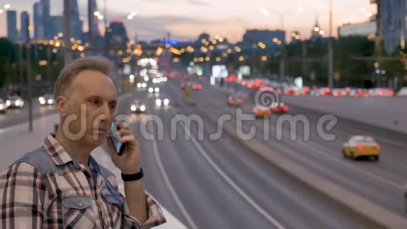 男人用手机对着黄昏的城市落日天空说话视频的预览图