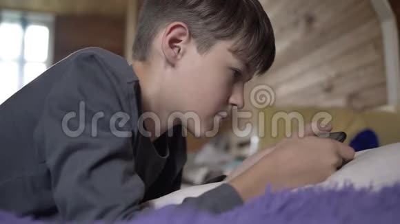 男孩躺在床上用电话青少年和朋友聊天玩游戏玩得开心视频的预览图