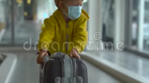 戴着医用口罩在机场玩手提箱的小男孩视频的预览图