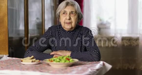 一位皱纹很深的老妇人坐在桌子旁等着吃午饭视频的预览图