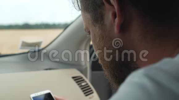 一个留着胡子的人坐在汽车的前排座位上看着电话4k4k视频视频的预览图