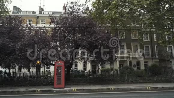 伦敦传统的红色电话亭站在靠近马路的街道上靠在树上国家标志视频的预览图
