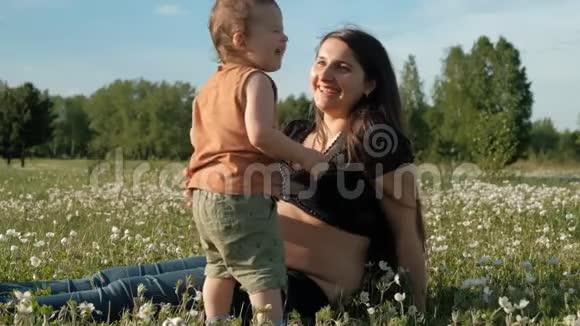 年轻漂亮的女人和她的儿子正坐在公园的草地上笑视频的预览图
