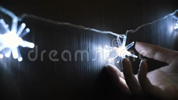 一个女孩的手拿着闪亮的白色星星形状的圣诞灯挂在黑色的墙上概念特写镜头视频的预览图