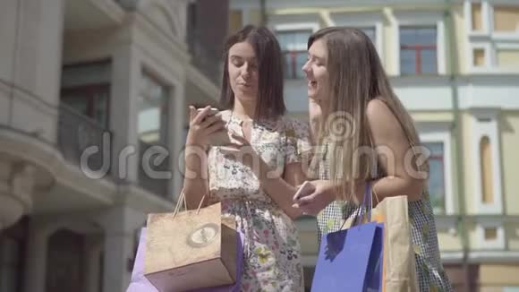 两个可爱的快乐女朋友在买完购物袋后在美丽的面前用手机发短信视频的预览图