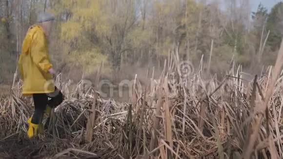 穿着黄色靴子和外套的人在沼泽中小心翼翼地行走视频的预览图
