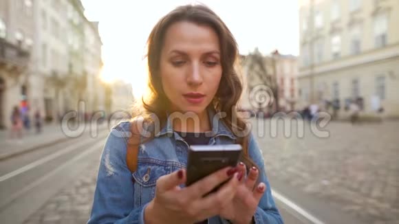 年轻的女人走在一条老街上用智能手机她很高兴看到那里赢或好运的概念视频的预览图