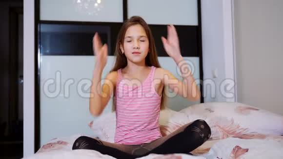 年轻女孩双手抱着坐在床上的莲花姿势视频的预览图