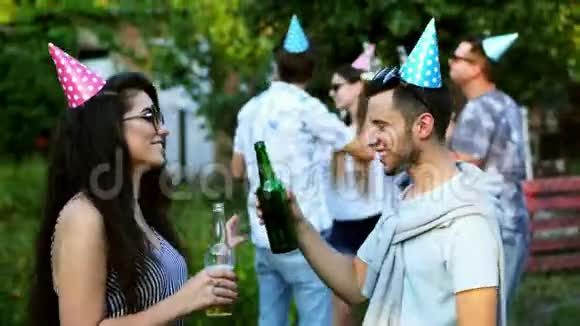 两个快乐的朋友跳舞聊天男人和女人在夏天的聚会上喝啤酒背景上的人穿着视频的预览图