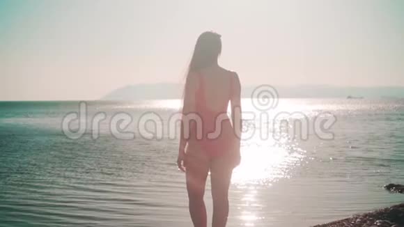 一个穿红色一件泳衣的女孩站在海滨一个女孩站起来举起双手显示出自由的迹象视频的预览图