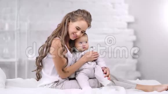 微笑迷人的母亲拥抱小婴儿感觉到爱被晨光包围在卧室里视频的预览图