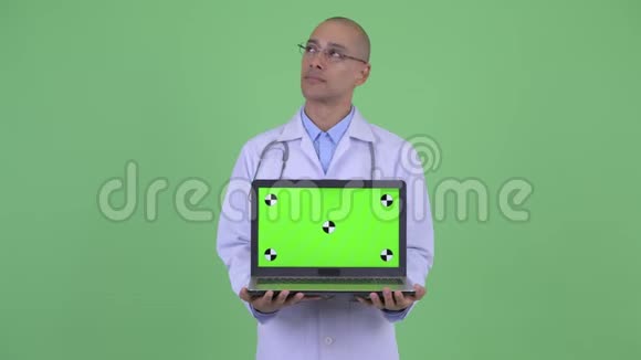 快乐的秃头多民族医生一边看笔记本电脑一边思考视频的预览图