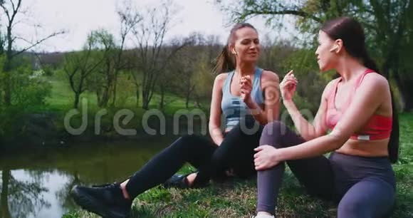 美丽的女士们经过艰苦的锻炼后笑容满面地坐在草地上一边笑着聊天视频的预览图