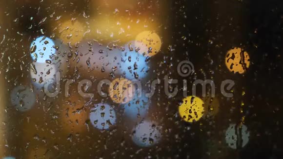 在晚上窗外模糊的光斑和落在玻璃上的雨滴的特写概念视频的预览图