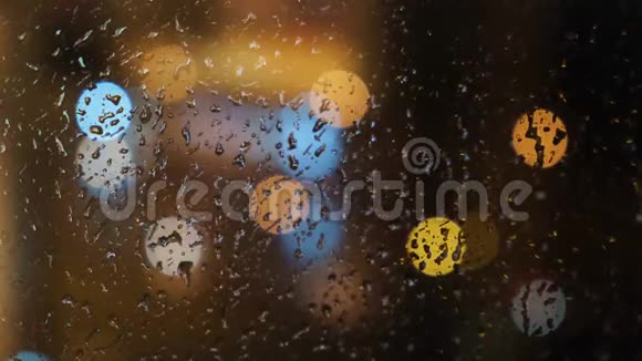 在晚上窗外模糊的光斑和落在玻璃上的雨滴的特写概念视频的预览图