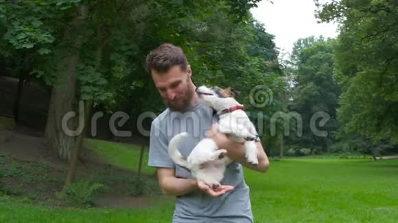 一个蓄着胡须的年轻人正抱着他心爱的狗杰克罗素梗在院子里享受着一个共同的休息视频的预览图