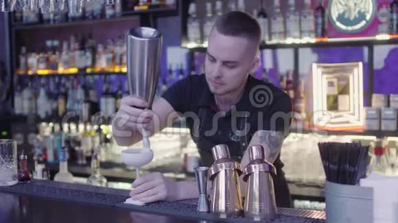 年轻的酒吧侍者站在酒吧柜台上用一杯奶油鸡尾酒在烤架上烤着一只小猕猴桃长架视频的预览图