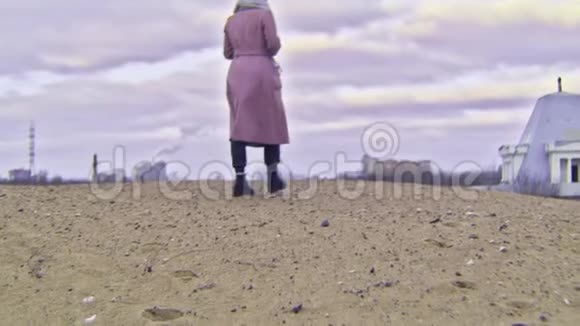 在秋天的城市和天空的背景下女人在沙滩上行走库存录像穿外套的漂亮女人的后景视频的预览图