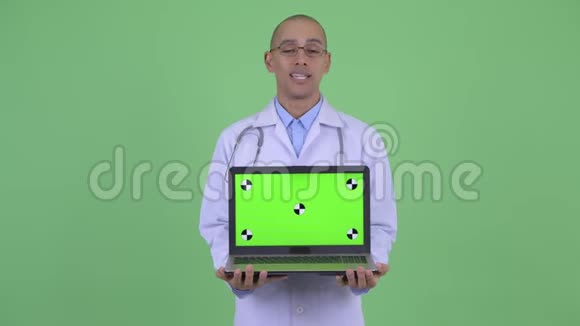 快乐的秃头多民族医生一边说话一边显示笔记本电脑视频的预览图