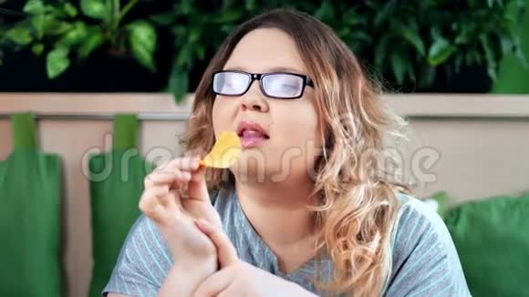 一幅令人愉快的胖女人吃不健康的薯片的肖像带着积极的情绪看着镜头视频的预览图