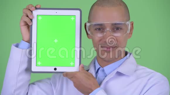 戴着防护眼镜显示数字平板电脑的快乐秃顶多民族医生脸视频的预览图