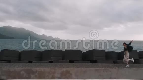 空中景观一个时髦的女孩沿着混凝土路堤在巨大的方形石头和背景下奔跑视频的预览图