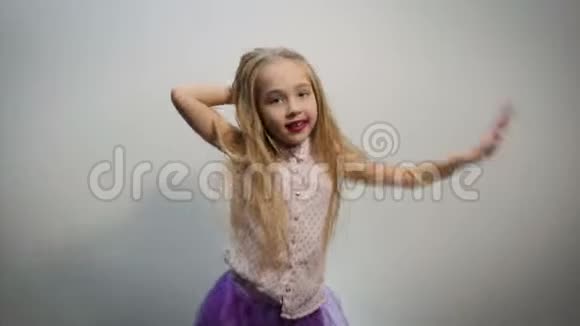 有趣的女孩宝贝穿着一件浅色衬衫的金发女郎上面有粉红色的圆点图案和紫色的色调连衣裙表演舞蹈动作视频的预览图