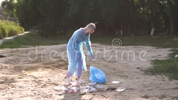 一个戴手套的志愿者女孩用垃圾袋收集海滩上的垃圾视频的预览图