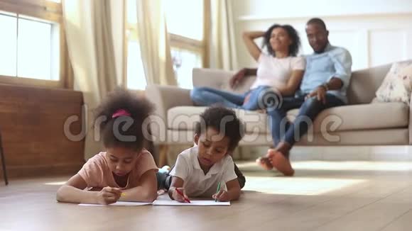 当父母在沙发上休息时孩子们在温暖的地板上画画视频的预览图