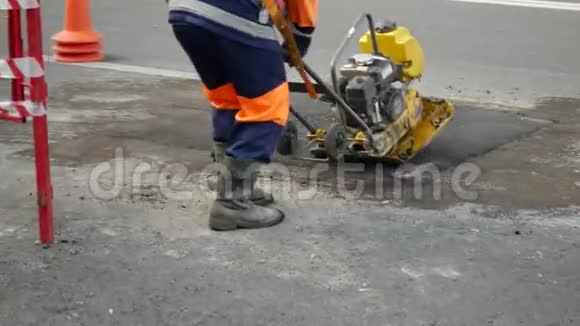 穿着橙色防护制服的人用刚铺好的沥青路面夯实视频的预览图