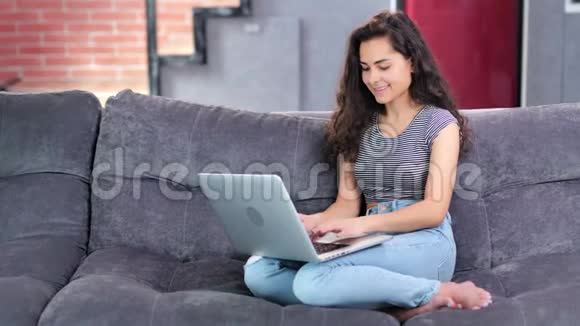 在客厅里坐在沙发上用手提电脑聊天笑得可爱的年轻女人满口都是视频的预览图