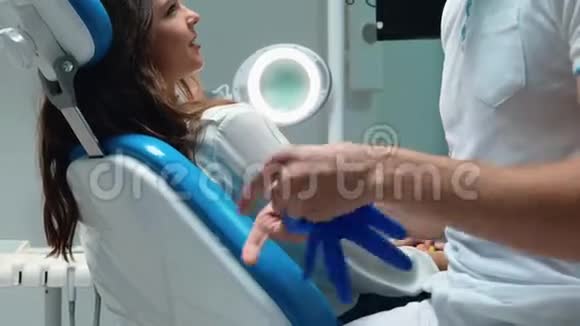 年轻的牙医在检查年轻的黑发女子病人之前戴着医用手套视频的预览图