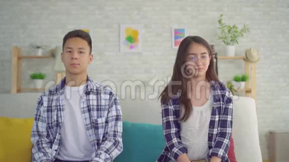 害羞的亚洲年轻女子和亚洲年轻男子坐在沙发上挨着对方视频的预览图