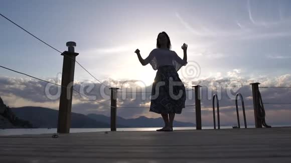 日出时一个穿着茂盛裙子的黑发女人在海边跳舞动作缓慢视频的预览图