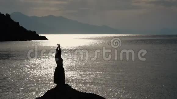 日落时分那个美丽的女人在海边的一块岩石上缓慢地跳舞视频的预览图