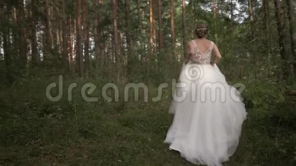 美丽的年轻开朗快乐的新娘穿着婚纱在树林里奔跑和旋转她跑开了视频的预览图