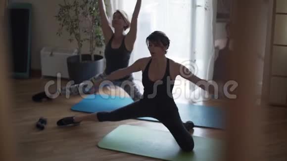 两个成熟的白种人妇女在家里的垫子上在地板上做运动女运动员伸展身体健康视频的预览图