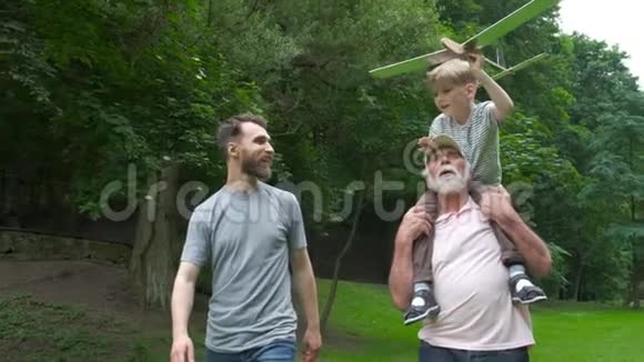 有飞机模型的小男孩和祖父在绿色公园的背景下举手享受生活和自然视频的预览图