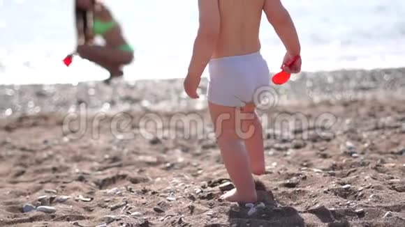 一个小婴儿沿着海滩散步带着一把铲子缓慢地走向大海视频的预览图