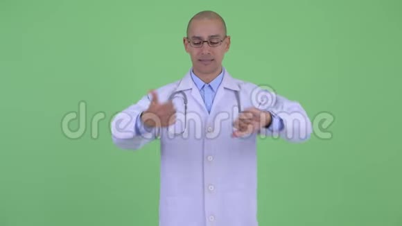 困惑的秃头多民族医生在拇指向上和拇指向下之间做出选择视频的预览图