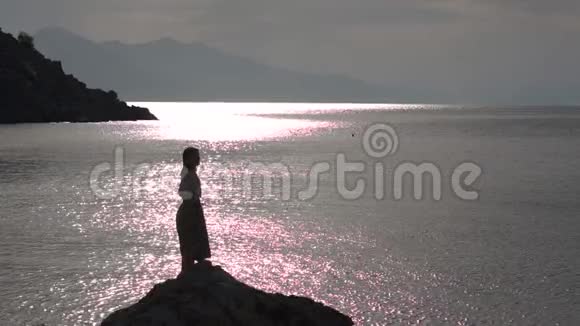 日出时女孩在海边的岩石上缓慢地举起双手视频的预览图