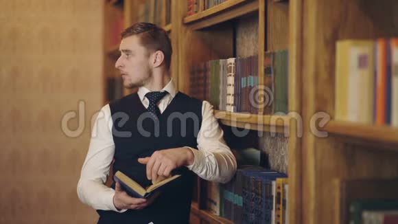 男记者在书架附近为文章阅读书籍制作研究聪明的作家拿着书分析视频的预览图