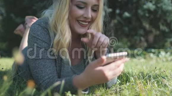 快乐女孩浏览智能手机躺在草坪上视频的预览图