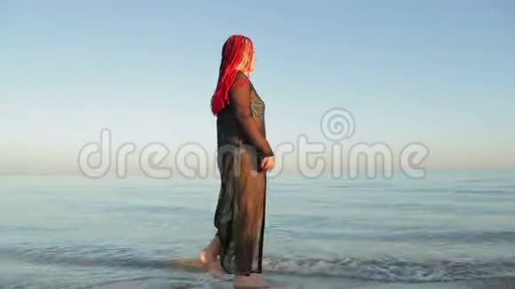 一个穿着泳衣穿着黑袍的女人在海边散步视频的预览图