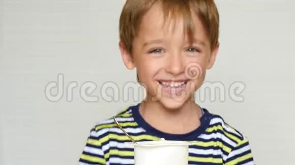 一个笑的男孩的肖像快乐的小男孩一边吃酸奶一边坐在桌子旁看着相机视频的预览图