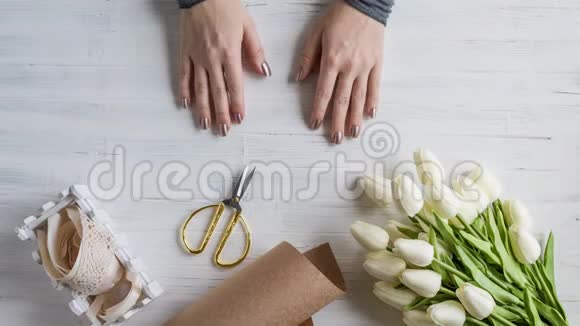 8一个女人花店把美丽的白色郁金香花束包装在木桌上的手工纸上送给情人视频的预览图