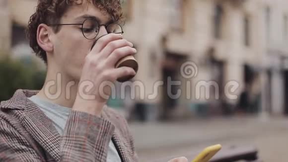 特写学生穿着夹克和眼镜喝着咖啡嘲笑他的现代手机屏幕男子视频的预览图